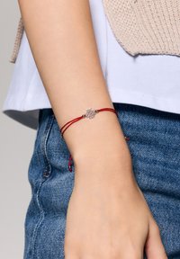 Czerwony regulowany sznurkowy bransoletka z centralnym srebrnym kwiatuszkiem i małymi metalicznymi akcentami po obu stronach.