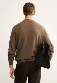 Brauner Strickpullover mit langen Ärmeln, kombiniert mit dunklen Hosen. Eine schwarze Wildledertasche hängt über der Schulter und hat eine strukturierte Oberfläche.