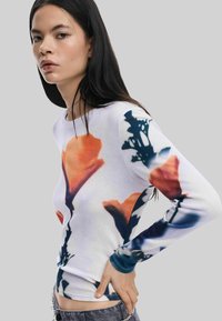 Langd袖top in witte stof met een abstract bloemenpatroon in oranje en blauw. Ronde hals en aansluitende pasvorm.