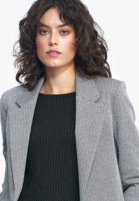 Marynarka w wzór houndstooth w czerni i bieli, z wyraźnym kołnierzem i dopasowanym krojem, nałożona na czarny, prążkowany top.