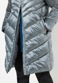 Giacca a vento argento con motivo a zigzag, dotata di chiusura con zip, tasche laterali e un morbido rivestimento interno visibile attraverso la parte anteriore aperta.