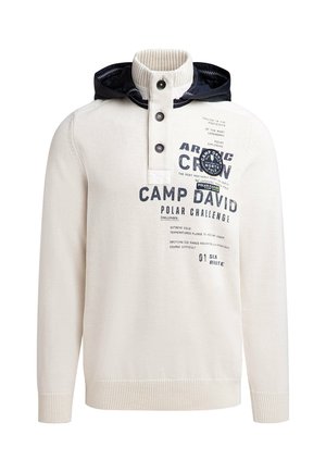Light cream sweater with a knitted texture, high collar, navy hood, button placket, and graphic text on the front.
