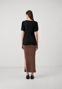 Top negru cu striații și mâneci scurte cu volane, asortat cu o fustă lungă din material cu striații de culoare maro, ce are o fante laterală. Modelul poartă pantofi negri.