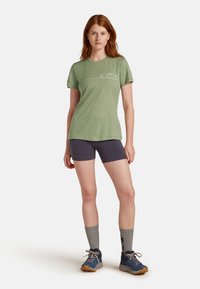 Lys grøn kortærmet t-shirt med et campingmotiv, sammen med mørke shorts og blå vandresko, der har grå sokker.