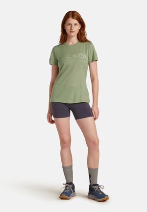 Hellgrünes Kurzarm-T-Shirt mit einem Campingmotiv, kombiniert mit dunklen Shorts und blauen Wanderschuhen, dazu graue Socken.