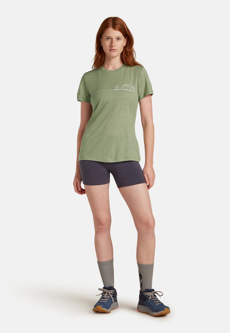 Lys grøn kortærmet t-shirt med et campingmotiv, sammen med mørke shorts og blå vandresko, der har grå sokker.