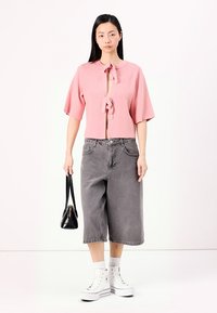 Ružový, krátkopy sleeves pletený top s viazaním a otvoreným predkom, skombinovaný so šedými širokými šortkami, bielymi teniskami a čiernou kabelkou.