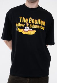 Black cotton T-shirt featuring a colorful graphic of a yellow submarine with the text "The Beatles Yellow Submarine" in bold, playful fonts.
