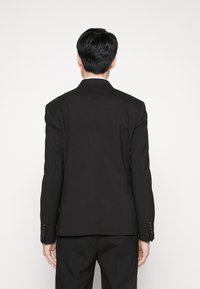 Chaqueta de traje negra ajustada, diseño estructurado, abertura sencilla en la parte trasera, tejido texturizado, puños con cuatro botones, corte Slim, acabado suave.
