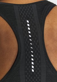 Detailní záběr na černou texturovanou sportovní podprsenku ze zadní strany s reflexním vertikálním pruhem na tmavé pleti.