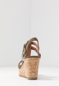 Sandale en liège à talon compensé de couleur vert olive avec une sangle réglable, présentant un design ouvert à l'arrière et des détails texturés en liège sur le talon.