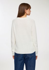 Biały sweter dzianinowy z okrągłym, ściąganym dekoltem, długimi rękawami raglanowymi i nieco luźnym krojem, w zestawieniu z niebieskimi dżinsami z wysokim stanem.