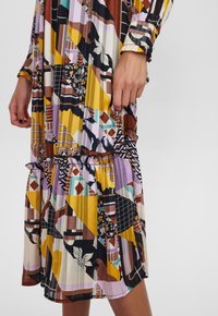 Robe multicolore à motifs géométriques avec un ourlet à volants à étages. Dotée de manches longues et d'une taille élastiquée, fabriquée en tissu léger.