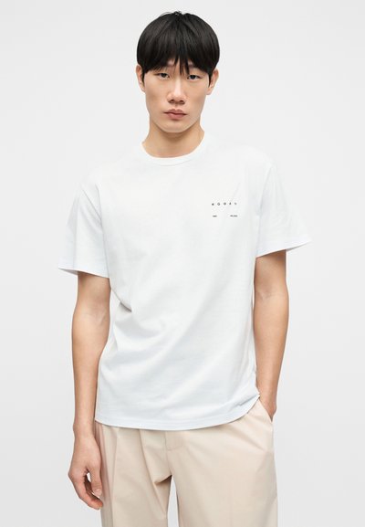 Λευκό βαμβακερό t-shirt με κοντά μανίκια. Διαθέτει μικρό μαύρο κείμενο-λογότυπο στο αριστερό στήθος. Απλός, κλασικός στρογγυλός λαιμός.