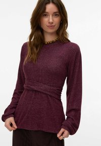 Dolga majica z dolgimi rokavi, globoko bordo barve, izdelana iz teksturirane tkanine, z zoženim pasom in sproščenimi rokavi, v kombinaciji z okroglim lesenim ogrlico iz kroglic.