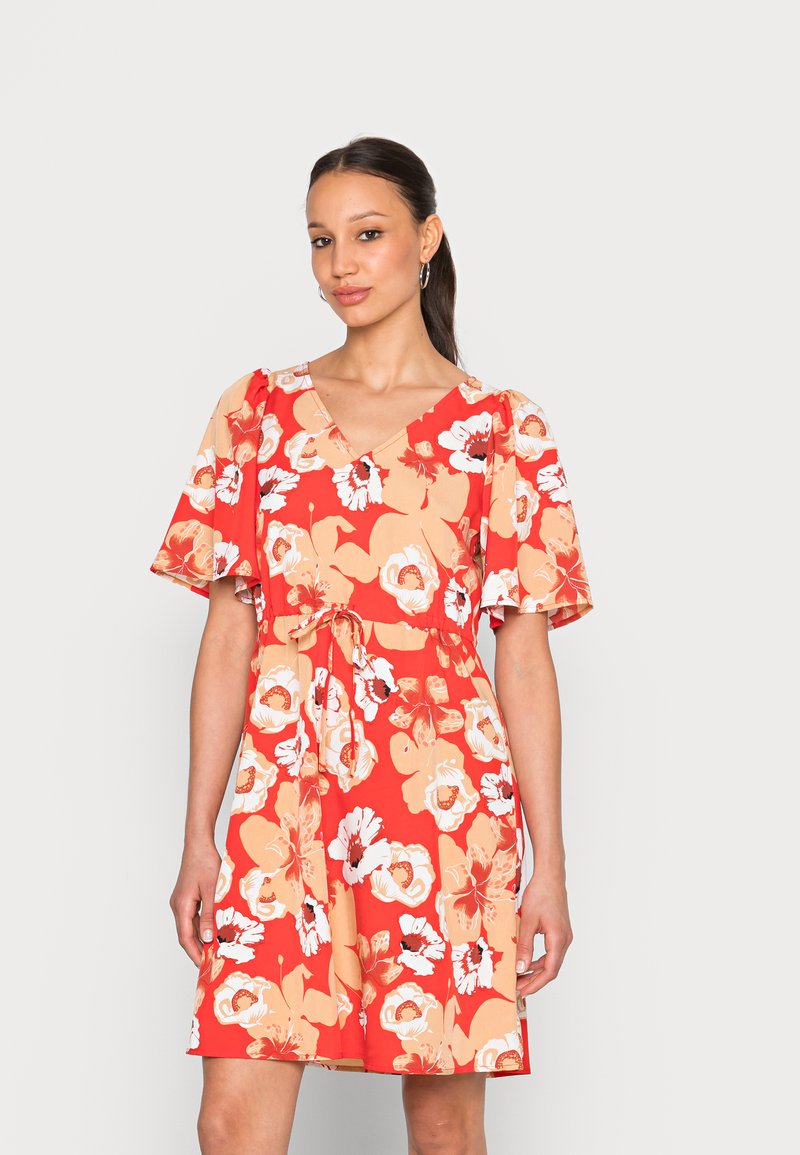 Vestido floral vermelho com decote em V, mangas curtas e onduladas, e cintura ajustada. Apresenta grandes flores brancas e pêssego em um fundo vibrante.