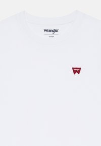 Bílé bavlněné tričko s kulatým výstřihem, na levé straně s malou červenou nášivkou loga Wrangler.