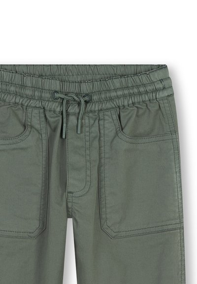 Pantalons verts à taille élastique avec cordon de serrage, poches avant et couture visible. Le matériau semble lisse avec une finition mate.