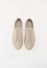 Beige lærstoff sneakers med en glatt tekstur, rund tå og lys brun gummisåle. Har flate lisser og preget merkeinnside.