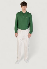 Grünes Langarm-Polohemd mit Kragen, kombiniert mit weißen Jogginghosen mit seitlichen Streifen und elastischem Bund, getragen mit weißen Turnschuhen.