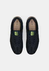Μαύρα αθλητικά παπούτσια με υλικά από δίχτυ και σουέτ. Διαθέτουν νεον πράσινες λεπτομέρειες, στρογγυλή μύτη και λαστιχένια σόλα. Ραφές σε όλο το παπούτσι.