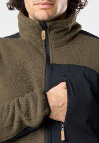 Fleecejacke für Herren mit hohem Kragen, ausgestattet mit kontrastierenden schwarzen Softshell-Akzenten und einer mit Reißverschluss versehenen Brusttasche. Strukturiertes, warmes Material.