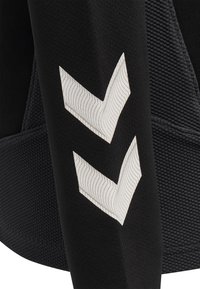 Sort sportsbeklædning med tekstureret stof og en glat strækpasform. To hvide chevron-designs på ærmet med subtile linjemønstre.