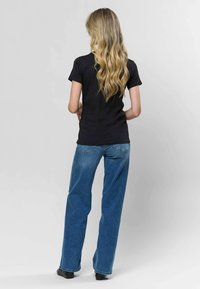 Melna īsām piedurknēm T-krekli, apvienots ar augsto jostasvīru zilajiem džinsiem; teksturēta auduma, brīvs piegriezums, minimālistisks dizains, bezšuvju apkakle.