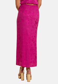 Jupe fuchsia en tissu texturé, de coupe longue et droite, dotée d'une fermeture éclair dissimulée au dos. Assortie à des chaussures à plateforme dorées chunky.