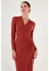 Robe rouge à manches longues avec un design croisé, présentant une texture drapée à la taille et un décolleté en V. Tissu lisse, silhouette ajustée.