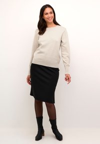 Pull en maille rayé beige et crème, associé à une jupe crayon noire. Porté avec des bottines noires, mettant en valeur une silhouette ajustée.