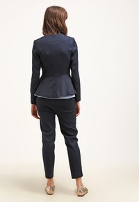 Granatowy, dopasowany garnitur z marynarką z baskinką i wąskimi spodniami, wykonany z teksturowanej tkaniny, dopełniony warstwową bluzką wystającą spod marynarki.