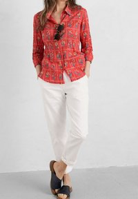Rood overhemd met knopen en bloemenprint, gestructureerde stof, opgerolde mouwen, gecombineerd met witte broek en zwarte slidesandalen. Eenvoudig ontwerp, casual pasvorm.