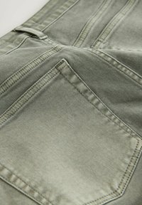 Gros plan sur un tissu en denim vert montrant des coutures détaillées et une poche arrière sur un pantalon.