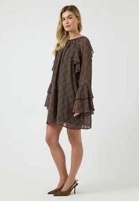 Brun rutemønstret kjole med lagdelte, rysjede ermer, rund hals og transparent materiale. Kombinert med brune spisse høye hæler.