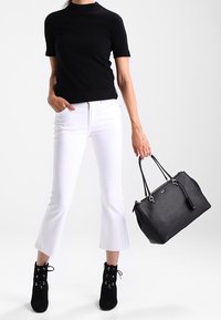 Svart kortärmad topp, vita utsvängda jeans, svarta ankelstövlar, håller en svart läderhandväska med dragkedja och silverdetaljer.