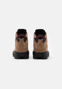 Paire de baskets montantes marron et noires avec des accents rouges, vue arrière montrant le logo "Air" sur le talon.