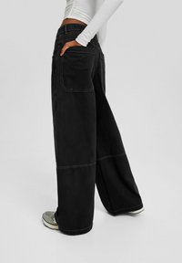 Wide-leg black jeans made of denim, featuring contrasting stitching, side pockets, and a back pocket with a logo detail.