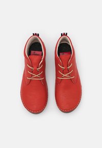 Chaussures en cuir rouge avec des lacets beiges, bout arrondi et coutures contrastées. Doublure intérieure douce et languette avec des accents rouges, blancs et bleus.