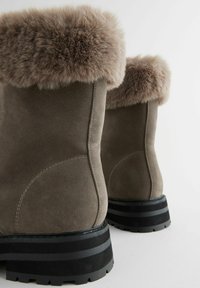 Grau Wildleder Stiefeletten mit einem kuscheligen grauen ;Fellkragen und einer schwarz gestreiften Gummisohle, die durch eine saubere Naht an der Seite hervorsticht.