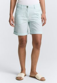 Shorts en coton bleu clair avec des ourlets roulés, des poches latérales et un unique bouton à l'avant. Associés à des sandales à glissière beige clair.