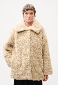 Beeži faux fur mantli lai krae, ülekandeline istuvus, pikad varrukad ja tekstuurne, karvane pind. Omab esipoolte taskuid.