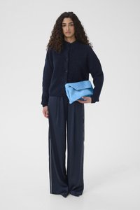 Cardigan en maille bleu marine avec boutons, coupe ample ; pantalon en satin bleu marine avec bandes latérales ; pochette texturée bleue tenue dans une main.