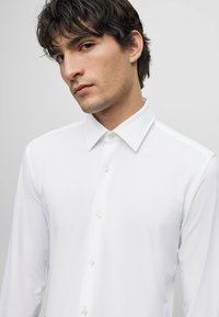 Camisa de dress blanca de manga larga con cuello clásico, con una textura suave y cierre de botones en el frente.