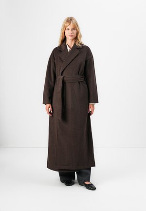 Brun, lang ullfrakk med belte i midjen, brede slag og lange ermer; har en teksturert overflate og minimalistisk design.