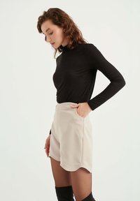 Zwarte long sleeve top met een slim fit, gecombineerd met beige high-waisted shorts en doorschijnende zwarte mailloze panty, met zijzakken en een gebogen zoom.