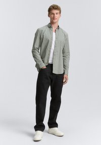 Chemise à boutons verte avec un motif géométrique, associée à un jean noir et des baskets blanches. Tissu lisse, coupe décontractée.