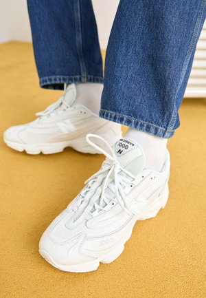 Witte New Balance 1000 sneakers van mesh en leer, met een ronde neus, gestructureerd ontwerp en veters. Gecombineerd met blauwe spijkerbroek.