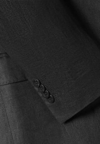 Rękaw czarnej marynarki z teksturowanej tkaniny, cztery czarne guziki oraz dopasowany krój z widocznymi detalami szwów.