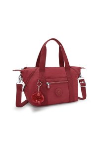 Red fabric bag with zippered pockets, short handles, and an adjustable strap. Features a charm and a logo patch on the side.